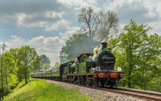 steam train on countryside railway track with green carriages